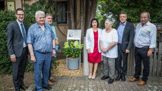 Oberbürgermeister Manuel Just (v.l.), Franz Piva, Initiator Friedrich Scheurich, Stella Kirgiane Efremidou (Pro West), Frida Mohr, Erster Bürgermeister Torsten Fetzner und Franz Schalk, ehemaliger Präsident des TuS Niederkirchen bei der Enthüllung der Gedenktafel für Heidi Mohr an ihrem Wohnhaus im Kurbrunnenweg.