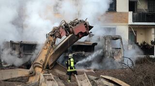Ein Feuerwehrmann löscht das brennende Wrack eines Lkw. Der 25 Tonnen schwere Bagger im Vordergrund wurde durch die Explosion im Jahr 2014 umgeworfen.