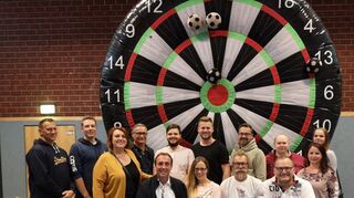 CCW-Vorstandsmitglieder, Senat und Aktive der Pro Spirit Allstars sitzen auf einem neuen Bodenläufer vor dem Fußball-Dart.
