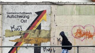 Ein Passant geht in Magdeburg an einem aus der Wendezeit stammenden verwitterten Wandbild mit dem Schriftzug „Gemeinschaftswerk Aufschwung Ost“ vorbei. Ostdeutsche sind in Spitzenpositionen bis heute unterrepräsentiert.