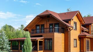 Beautiful luxury big wooden house. Timber cottage villa with with green lawn, garden and blue sky on background.