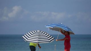 Ein Paar baut zwei Schirme am Strand auf Mallorca auf, um sich vor der Sonne zu schützen. Sand reflektiert das Licht und verstärkt die UV-Strahlung.