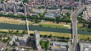 Zwischen den Berufsschulen und der Zufahrt zur Friedrich-Ebert-Brücke gelegen: Das Areal Schafweide, derzeit mit Bäumen bewachsener Parkplatz, Brachfläche und Standort von einem Kiosk.