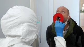 Eine Mitarbeiterin nimmt im Schnelltestcenter in Ludwigshafen durch ein Loch in der Scheibe den Rachenabstrich bei Michael Callies vor.