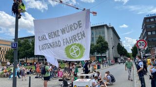 Circa 30 Menschen blockierten die Straße in den Quadraten mit Bannern. Zwei von ihnen waren auf Masten geklettert.