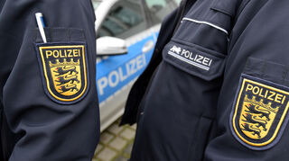 Zwei Wappen der baden-württembergischen Polizei sind am neben einem Polizeifahrzeug zu sehen.