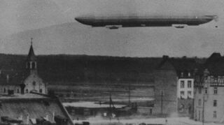 Luftschiff über dem Marktplatz Mannheim-Rheinau. Vor der Kirche zu erkennen: ein Mann, der zur besseren Sicht auf ein Dach gestiegen ist.