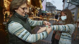 Christiane Huth (li.) legt Celine Morin auf dem Wormser Weihnachtsmarkt das grüne Bändchen als Geimpft-Nachweis an.