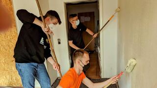 Lennart (l.), Timo (hinten) und Noah (vorne) greifen zur Malerrolle, um Wohnräume der Kirchengemeinde für Flüchtlinge aus der Ukraine herzurichten.