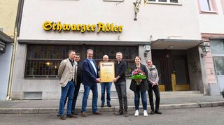 Unter dem Schriftzug und dem historischen Messingschild: Holger Vatter-Schönthal (v. l.) , Hendrik Kießl und Andreas Hiby-Durst von Eichbaum übergeben die Urkunde an Walter, Christian, Claudia und Mary Oberthür, die seit Jahrzehnten die gutbürgerliche Gaststätte in D 6 führen.