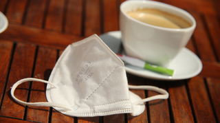 Eine FFP2-Maske liegt neben einer Tasse Kaffee auf einem Tisch. Am Sonntag fällt die Maskenpflicht in Innenräumen weg.
