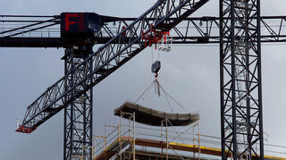 An einem Baukran wird Baumaterial auf der Baustelle transportiert. (Symbolbild)