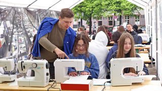 Schülerinnen schlüpfen in die Rolle von Arbeiterinnen in Textilfabriken: Vorarbeiter Mick Dolshenko (v.l.) schaut Shana und Anna über die Schulter.