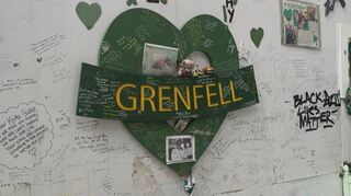 Vor dem Hochhaus im Westen Londons hängt an einer Mauer ein grünes Herz mit der Aufschrift „Grenfell“, daneben stehen handgeschriebene Botschaften.