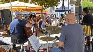 Die Honeysuckle Twins spielen auf der Bühne auf der Pfalzstraße, während das Publikum unter den Bäumen am Rathaus sitzt.
