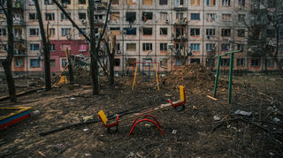 Ein Bild aus dem Ukraine-Krieg: Eine Wippe steht in einen leeren Kindergarten vor einem nach russischem Beschuss völlig zerstörten Gebäude.