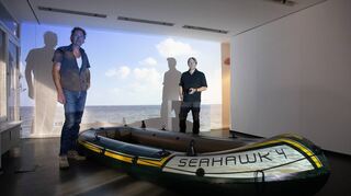 Ein idyllischer Strand und davor ein Schlauchboot – mehr braucht das Künstler-Duo Eric Carstensen (l.) und Michael Volkmer nicht, um vieles auszusagen.