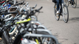 Eine Radfahrerin fährt an geparkten Fahrrädern vorbei.
