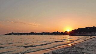 Von der Platja des Dolc aus rundet der Sonnenuntergang, der die Uferzeile von Colònia de Sant Jordi als Silhouette abzeichnet, einen entspannten Strandtag ab.