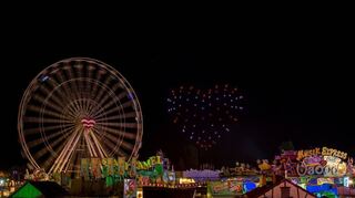 Drohnen zeigen ein Herz aus lauter Lichtpunkten neben dem Riesenrad.