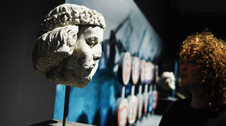 Eine Frau steht in den Reiss-Engelhorn-Museen in der Sonderausstellung "Die Normannen" neben einer Steinskulptur von Wilhelm der Eroberer aus dem 14 Jahrhundert.