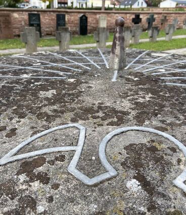 Alpha, Omega und eine Sonnenuhr auf dem Gedenkstein der Kriegsgräber auf dem Friedhof in Edingen.