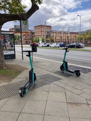 Ein taktiles Bodenleitsystem in der Nähe des Schlosses ist von zwei E-Tretrollern zugeparkt. Das bedeutet Gefahr und Erschwerung der Orientierung für blinde Menschen im öffentlichen Raum.