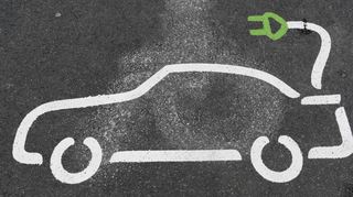 Ein Piktogramm eines Elektroautos ist auf einem Parkplatz an einer Ladestation auf dem Asphalt aufgemalt.