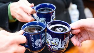 Drei Weihnachtsmarkt-Besucher stoßen mit Glühwein an.