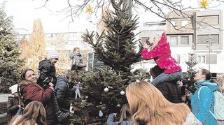 Kinder behängen die Tannenbäume auf dem Apostelplatz mit selbst gebastelten Kugeln und Figuren.