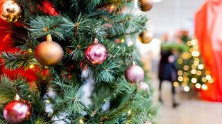Ein mit Weihnachtsbaumkugeln geschmückter Baum aus Kunststoff steht in einem Baumarkt zum Verkauf.