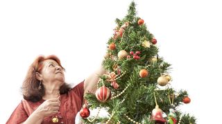 Latin mature woman decorating a Christmas tree at home. Low angle view with copy space.