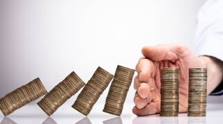 Close-up Of A Businessperson's Hand Protecting Stacked Coins From Falling On Reflective Desk