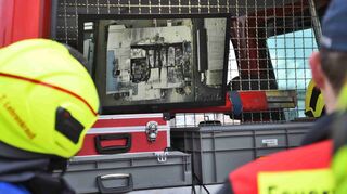Kräfte der Feuerwehr schauen sich Fotos an, die eine Drohne aus der Luft von der zerstörten Großbäckerei aufgenommen hat.