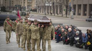 Menschen knien in Kiew nieder, während ukrainische Soldaten den Sarg eines im Krieg getöteten Kameraden bei einer Gedenkfeier tragen.
