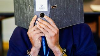 Der Angeklagte mit Handschellen verbirgt sein Gesicht hinter einem Aktenordner.
