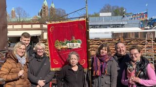 Die Speyerer Schausteller, die Damen von der Stadtverwaltung und ihre traditionelle Fahne vor der Kulisse des Doms.