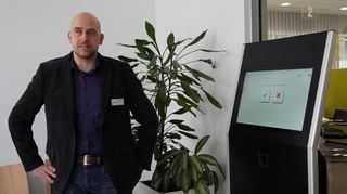 Jörg Gutperle neben dem Bildschirm, über den sich Besucher für ihren Termin im Bürgerbüro anmelden können.