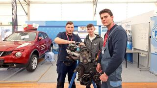 Azubi Salvatore Schiafone (v.l.), Geselle Finn Strohmer und Azubi Reinhard Kelm arbeiten am Motor am Stand der Kfz-Innung in der Handwerkshalle.