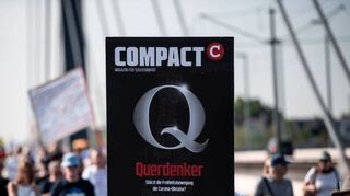 Teilnehmer einer Demonstration gegen die Corona-Maßnahmen halten in Düsseldorf ein Schild hoch, auf dem „Compact“ und „Querdenker“ steht.