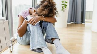 African-American girl is at home by the window. She is holding a mobile phone