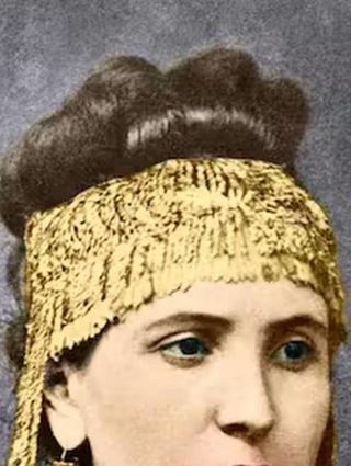 Seiner jungen Frau Sophia hängt Heinrich Schliemann den Schmuck aus dem Schatz des Priamos um und drapiert sie damit als „Schöne Helena“.