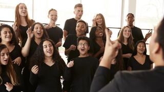 Male And Female Students Singing In Choir With Teacher At Performing Arts School