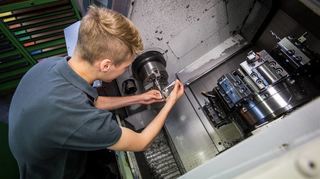 Symbolbild: Ein junger Werkzeugmechaniker arbeitet an einer Drehmaschine.