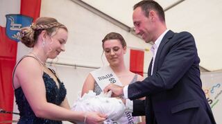 Krönungsmeister Konstantin Großmann setzt der neuen Gurkenkönigin Nina I. (Mitte) ihr Diadem auf, das Lenja bereit hält.