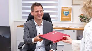 Sekretärin Daniela Weidler überreicht Thorsten Walther an seinem ersten Arbeitstag bereits wichtige Akten.