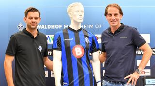 Sportgeschäftsführer Tim Schork (l.) und Trainer Rüdiger Rehm posieren mit dem Waldhof-Trikot,auf dem nun auch ein Sponsoren-Logo prangt.