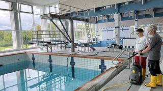 Zwei Mitarbeiterinnen bei der Grundreinigung am Rand des Schwimmerbeckens im Freizeitbad der Gemeinde.
