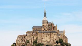Wie aus dem Felsen herausgewachsen: die Klosterburg Mont Saint-Michel an der Küste der Normandie, im Vordergrund die Fußgängerbrücke.