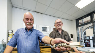Johannes Doerr und Remo Krembel, Brille, halten als Ehrenamtliche als "Dinosaurier des Druckerberufs" die Maschinen am laufen und warten und reparieren sie. Doerr setzt gerade einige Worte zusammen und Krembel rührt Druckfarbe an.
